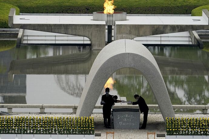 Two men, one standing and one bowing, pictured under a memorial arch.